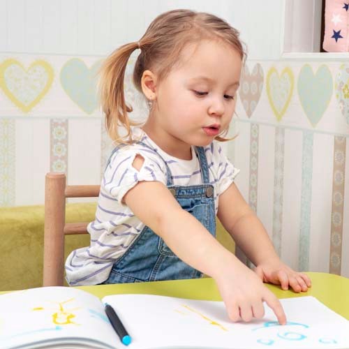 little beautiful girl points to her drawing sitting at the table in the nursery