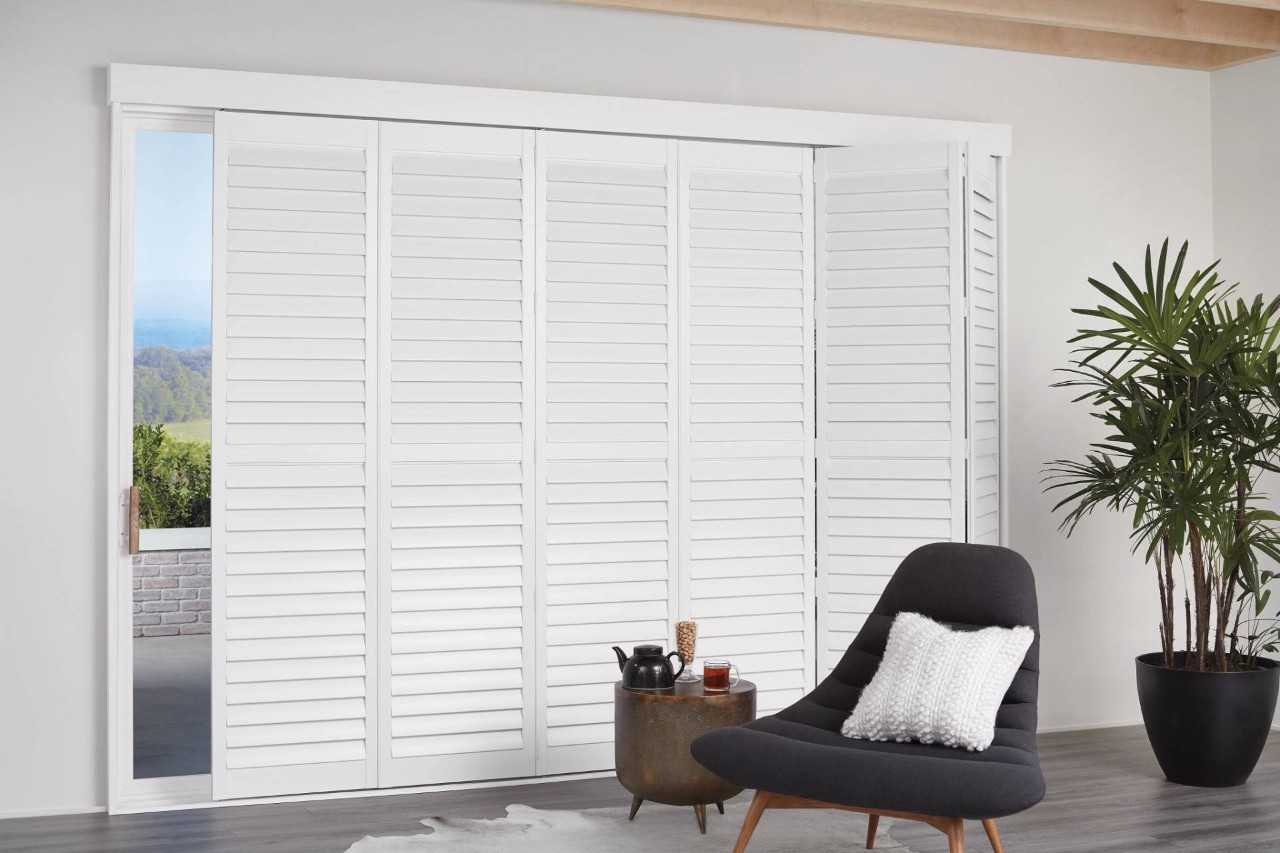 Home living room with a sliding glass door covered with white Hunter Douglas NewStyle® Hybrid Shutters near Monroeville, PA