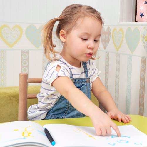 little beautiful girl points to her drawing sitting at the table in the nursery