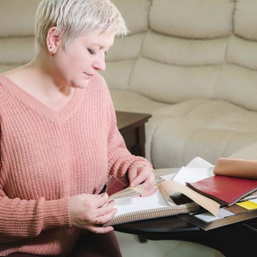 Portrait of an attractive mature short-haired woman in a pink sweater sits in a leather armchair in a furniture store and selects the color and upholstery material of the furniture. Looks at textile samples.